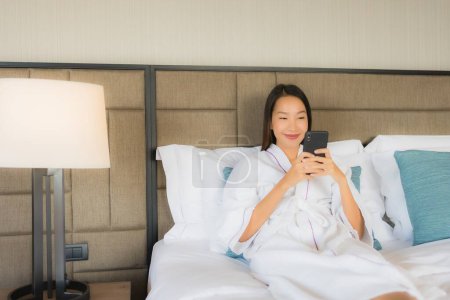 Foto de Retrato hermosa joven asiático mujeres utilizando teléfono inteligente móvil con taza de café en la cama en el interior del dormitorio - Imagen libre de derechos