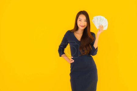 Foto de Retrato hermosa joven asiática mujer con dinero y dinero en efectivo en amarillo aislado fondo - Imagen libre de derechos
