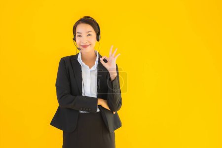 Photo for Portrait beautiful young business asian woman with headphone or headset for call center or telemarketing on yellow isolated background - Royalty Free Image