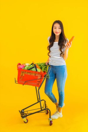 Téléchargez les photos : Portrait belle jeune asiatique femme shopping épicerie de supermarché et chariot sur fond jaune isolé - en image libre de droit