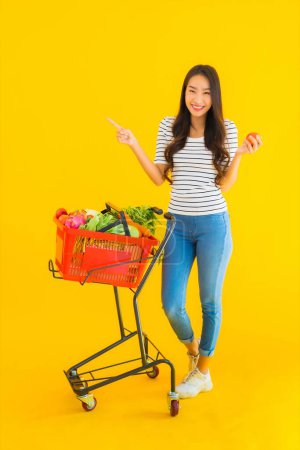 Foto de Retrato hermosa joven asiática mujer compras tienda de comestibles de supermercado y carro en amarillo aislado fondo - Imagen libre de derechos