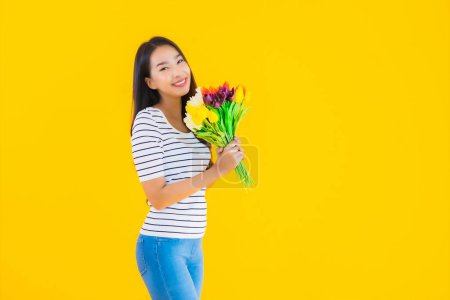 Téléchargez les photos : Portrait belle jeune femme asiatique avec fleur colorée sur fond jaune isolé - en image libre de droit
