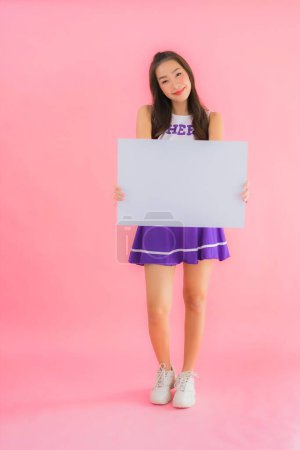 Photo for Portrait beautiful young asian woman cheerleader smile show empty white board on isolated pink background - Royalty Free Image