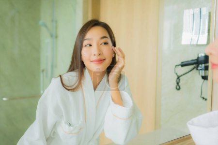Téléchargez les photos : Portrait belle jeune femme asiatique check up visage dans salle de bain intérieur - en image libre de droit