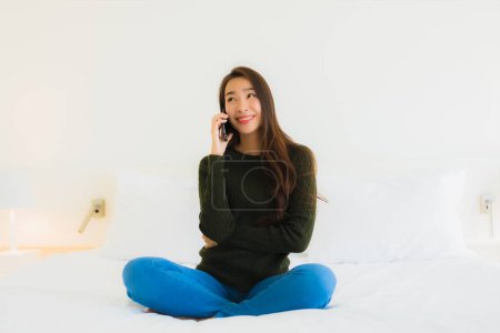 Téléchargez les photos : Portrait belle jeune femme asiatique utiliser téléphone mobile intelligent sur le lit avec couverture d'oreiller blanc dans l'intérieur de la chambre - en image libre de droit