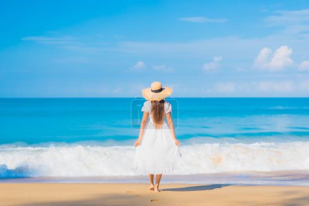 Foto de Retrato hermosa joven asiática mujer relajarse sonrisa ocio alrededor mar playa océano con blanco nube en azul cielo en viaje vacaciones - Imagen libre de derechos