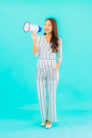 Téléchargez les photos : Portrait belle jeune femme asiatique utiliser mégaphone pour la communication sur fond bleu isolé - en image libre de droit