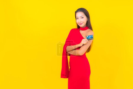 Téléchargez les photos : Portrait belle jeune femme asiatique avec carte de crédit sur fond jaune - en image libre de droit
