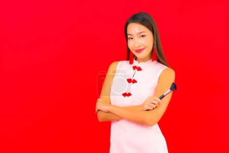 Téléchargez les photos : Portrait belle jeune femme asiatique avec maquillage pinceau cosmétique sur fond rouge isolé - en image libre de droit