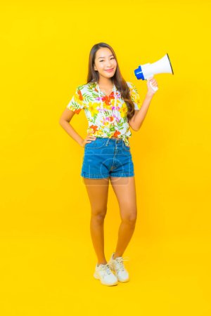 Photo pour Portrait belle jeune femme asiatique utiliser mégaphone pour la communication sur fond jaune - image libre de droit