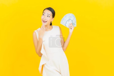 Foto de Retrato hermosa joven asiática mujer sonrisa con un montón de dinero en efectivo y dinero en color amarillo fondo - Imagen libre de derechos