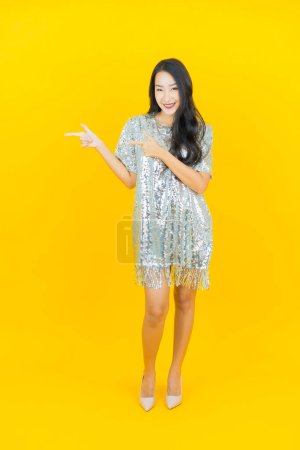 Téléchargez les photos : Portrait belle jeune femme asiatique sourire avec action sur fond de couleur jaune - en image libre de droit