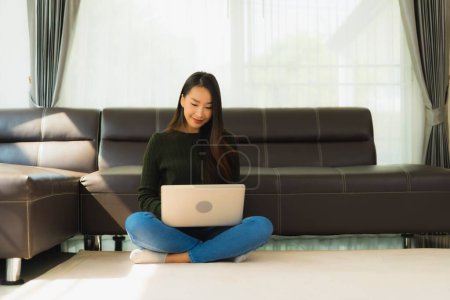 Téléchargez les photos : Portrait belle jeune femme asiatique utiliser ordinateur portable avec canapé dans le salon intérieur - en image libre de droit