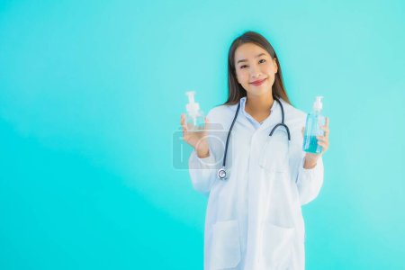 Téléchargez les photos : Portrait belle jeune femme asiatique médecin avec de l'alcool gel pour la main propre et protéger de covid19 ou coronavirus sur fond bleu isolé - en image libre de droit