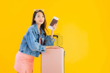 Foto de Retrato hermosa joven asiática mujer con equipaje bolsa de viaje con pasaporte y billete de embarque en amarillo aislado fondo - Imagen libre de derechos