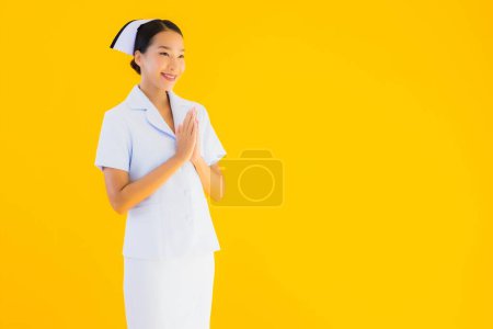 Téléchargez les photos : Portrait belle jeune asiatique thai infirmière sawasdee ou dire bonjour en thaï sur fond jaune isolé - en image libre de droit