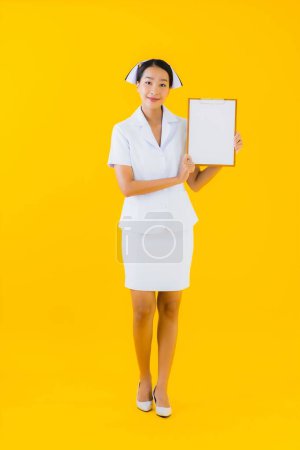 Photo for Portrait beautiful young asian woman thai nurse show empty white board and work at clinic or hospital on yellow isolated background - Royalty Free Image