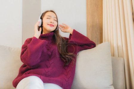 Téléchargez les photos : Portrait belle jeune femme asiatique utiliser casque pour écouter de la musique sur canapé dans le salon intérieur - en image libre de droit