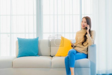 Foto de Retrato hermosa joven mujer asiática con teléfono móvil inteligente en el sofá en el interior de la sala de estar - Imagen libre de derechos