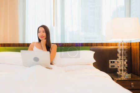 Téléchargez les photos : Portrait belle jeune femme asiatique utiliser ordinateur portable sur le lit dans la chambre à coucher intérieur - en image libre de droit
