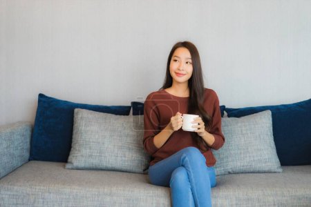 Téléchargez les photos : Portrait belle jeune femme asiatique relax sourire sur canapé dans le salon intérieur - en image libre de droit