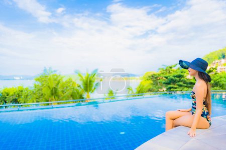 Téléchargez les photos : Portrait belle jeune femme asiatique relax sourire loisirs autour de la piscine extérieure avec vue sur l'océan de mer pour des vacances de voyage - en image libre de droit