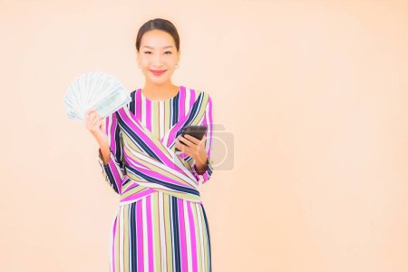 Photo for Portrait beautiful young asian woman with cash or money and mobile smart phone on color isolated background - Royalty Free Image