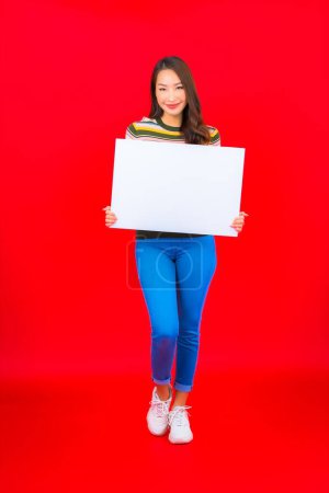 Téléchargez les photos : Portrait belle jeune femme asiatique avec panneau blanc vide sur fond rouge - en image libre de droit