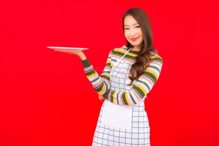 Téléchargez les photos : Portrait belle jeune femme asiatique montrer plat vide sur fond rouge - en image libre de droit