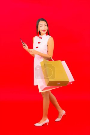 Téléchargez les photos : Portrait belle jeune femme asiatique avec sac à provisions coloré sur fond rouge isolé - en image libre de droit