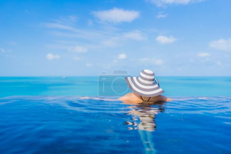 Foto de Retrato hermosa joven mujer asiática relajarse sonrisa ocio alrededor de la piscina al aire libre en resort hotel con vista al mar océano - Imagen libre de derechos