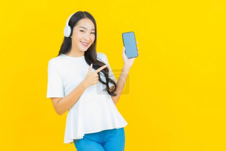 Foto de Retrato hermosa joven mujer asiática con auriculares y teléfono inteligente para escuchar música sobre fondo amarillo - Imagen libre de derechos