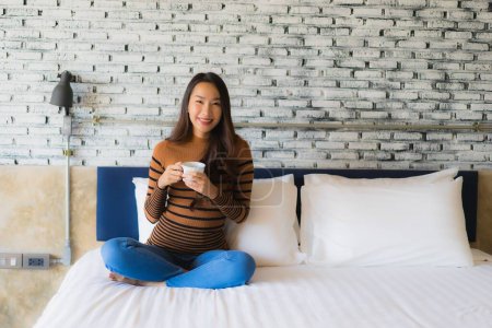 Foto de Joven mujer asiática con taza de café en la cama en el interior del dormitorio - Imagen libre de derechos
