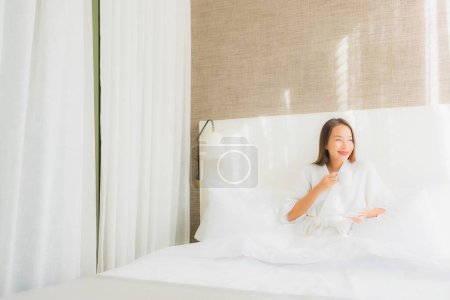 Foto de Retrato hermosa joven asiática mujer feliz sonrisa con taza de café en la cama en el interior del dormitorio - Imagen libre de derechos