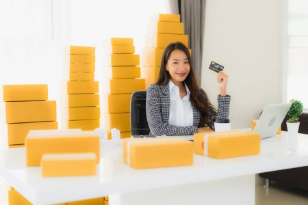 Téléchargez les photos : Portrait belle jeune femme asiatique travailler de la maison avec carte de crédit et boîte en carton prêt pour l'expédition des achats en ligne - en image libre de droit
