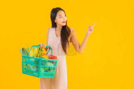Téléchargez les photos : Portrait belle jeune femme asiatique avec panier d'épicerie sac à provisions du supermarché avec carte de crédit sur fond jaune isolé - en image libre de droit