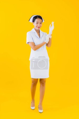 Téléchargez les photos : Portrait belle jeune femme asiatique thai infirmière porter gant sur fond jaune isolé - en image libre de droit