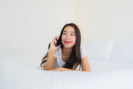 Foto de Retrato hermosa joven mujer asiática utilizar el teléfono móvil inteligente en la cama con manta de almohada blanca en el interior del dormitorio - Imagen libre de derechos