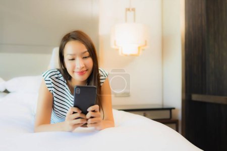 Photo for Portrait beautiful young asian woman use smart mobile phone on bed in bedroom interior - Royalty Free Image