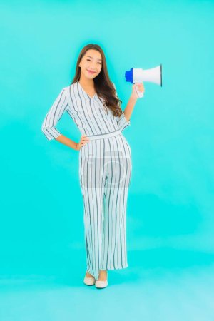 Téléchargez les photos : Portrait belle jeune femme asiatique utiliser mégaphone pour la communication sur fond bleu isolé - en image libre de droit
