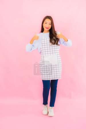 Foto de Retrato hermosa joven asiática mujer en ropa de cocina con delantal en rosa aislado fondo - Imagen libre de derechos