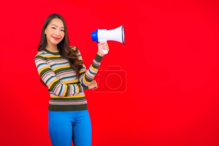 Téléchargez les photos : Portrait belle jeune femme asiatique avec mégaphone pour la communication sur fond rouge - en image libre de droit