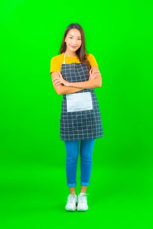 Foto de Retrato hermosa joven mujer asiática usar delantal con acción en verde aislado fondo - Imagen libre de derechos
