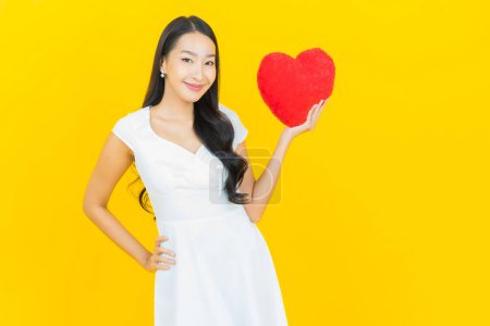 Photo for Portrait beautiful young asian woman smile with heart pillow shape on yellow color background - Royalty Free Image