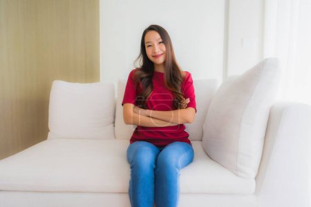 Téléchargez les photos : Portrait belle jeune asiatique femmes heureux sourire assis sur canapé chaise dans salon intérieur - en image libre de droit