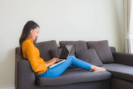Foto de Retrato de mujer asiática joven usando portátil cuaderno de notas en el sofá para el trabajo en la sala de estar - Imagen libre de derechos