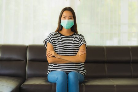 Téléchargez les photos : Portrait belle jeune femme asiatique avec masque rester à la maison sur canapé dans le salon pour protéger coronavirus ou covid19 - en image libre de droit