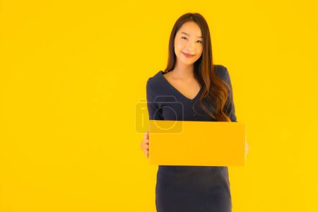 Téléchargez les photos : Portrait belle jeune femme asiatique avec boîte en carton packkage prêt pour l'expédition sur fond jaune isolé - en image libre de droit