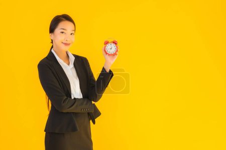 Photo for Portrait beautiful young asian woman show time of clock or alarm on yellow isolated background - Royalty Free Image