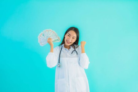 Photo for Portrait beautiful young asian doctor woman with a lot of cash and money on blue isolated background - Royalty Free Image